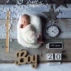 a baby wrapped in a blanket next to a clock and other items on a wooden table