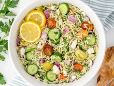 a white bowl filled with pasta salad next to sliced lemons and cucumbers