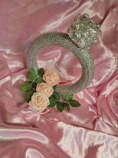 a tiara with three roses on it sitting on a pink satin surface next to a flower