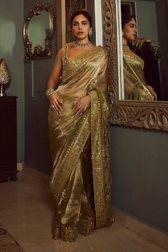 a woman standing in front of a mirror wearing a gold sari