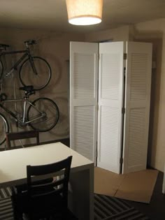 a bike is mounted to the wall next to a table and chair in a room with white shutters