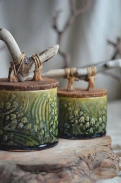 two ceramic containers sitting on top of a wooden table next to a tree branch with branches in the background