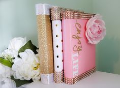 two books with pink covers are sitting on a white table next to flowers and a vase