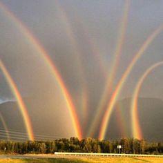 three rainbows in the sky over a highway with mountains in the backgroud