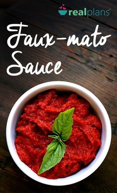 a white bowl filled with red sauce on top of a wooden table next to a green leaf