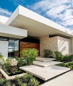 a modern house with plants and rocks in the front yard