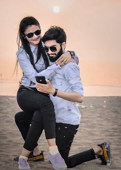 two people are hugging on the beach while one person is taking a selfie with his cell phone