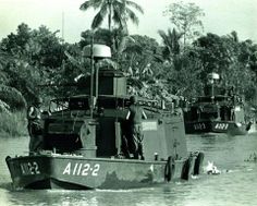 two men standing on top of a boat in the water next to trees and bushes