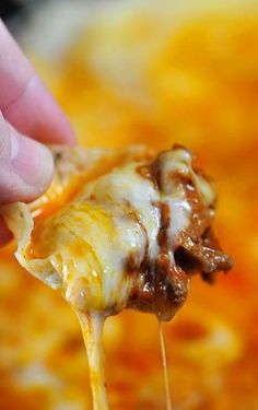 a hand holding a piece of cheese covered pizza