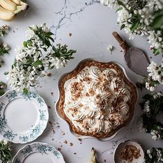 there is a pie with white frosting on it next to some bananas and flowers