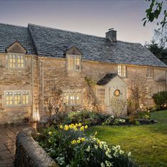 a large stone house with lots of windows and flowers in the front yard at night