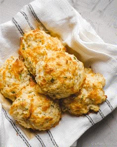 some biscuits are sitting on top of a white towel and napkin with the rest of the biscuits in it