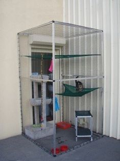 a cat is sitting on top of a cage in the corner of a room that's next to a building