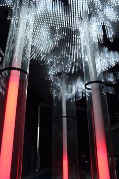 several tall glass vases are lit up with red light in the middle and white lights hanging from them