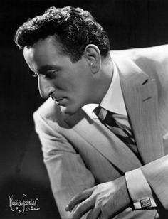 a black and white photo of a man in a suit with his hands on his knees