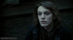 a man with long hair and blue eyes stares at the camera in a dark room