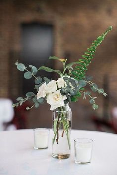 a vase filled with flowers and greenery sitting on top of a table next to two glasses