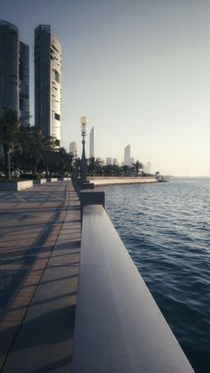 an empty pier next to the ocean with tall buildings in the background