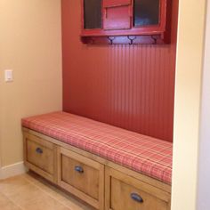 a wooden bench sitting in the corner of a room next to a red cabinet and window