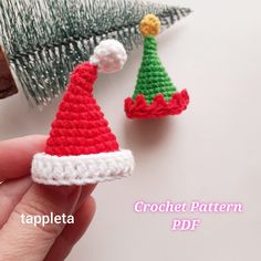 two crocheted christmas hats sitting on top of a table next to a needle