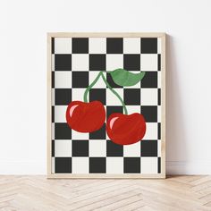 two cherries on a black and white checkered background are displayed in a wooden frame