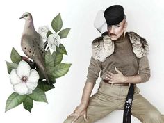 a man sitting next to a bird on top of a branch with flowers in it