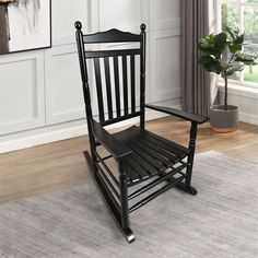 a black rocking chair sitting on top of a rug next to a potted plant