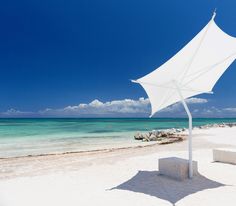 an umbrella sitting on top of a white sandy beach next to the ocean and blue sky