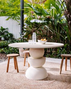 a white table and two stools in front of some plants