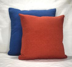 two orange and blue pillows on a white bed