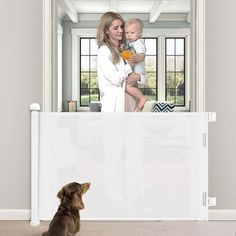 a woman holding a baby looking at her reflection in a mirror with a dog sitting on the floor