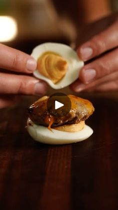 a person holding an open hard boiled egg on top of a bun covered in melted cheese