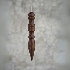 a small wooden wind chime hanging from a rope on a concrete wall behind it