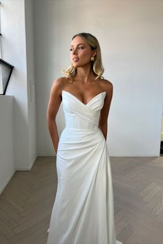 a woman in a white wedding dress standing next to a window with her hands on her hips