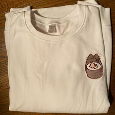 a white t - shirt with a small patch on the chest and a brown bear in it