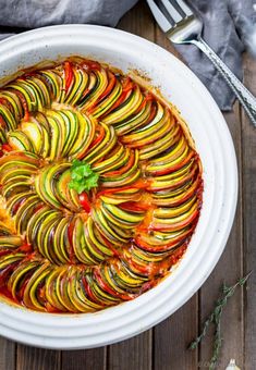 a white bowl filled with cooked vegetables on top of a wooden table next to utensils