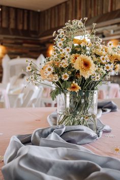 a vase filled with yellow and white flowers on top of a table covered in gray cloth