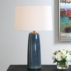 a blue vase sitting on top of a wooden table next to a lamp and flowers