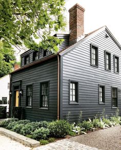 a gray house with black shutters on the front and side windows is surrounded by greenery