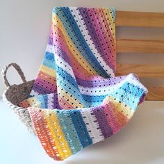 a crocheted blanket sitting on top of a wooden bench next to a basket