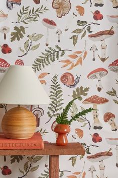 a lamp on top of a wooden table next to a wallpaper with mushrooms and leaves