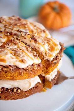 a cake with frosting and nuts on top sitting on a white plate next to an orange pumpkin