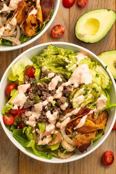 two bowls filled with lettuce, meat and vegetables on top of a wooden table