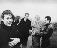 a group of people standing on top of a hill next to a tall stone pillar