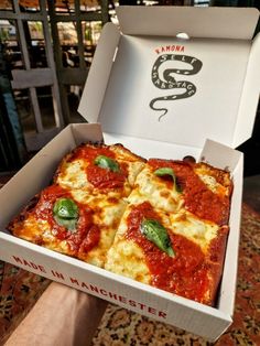 a person holding up a pizza in a box with pepperoni and cheese on it