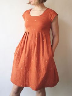 a woman standing in front of a wall wearing an orange dress with white dots on it