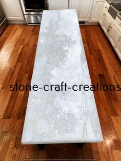 a long white marble bench sitting in the middle of a wood floored kitchen area