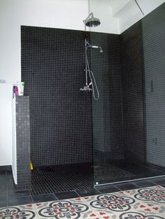 a walk in shower sitting next to a tiled floor and white wall with black tiles on it