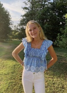 a woman standing in the grass with her hands on her hips and looking at the camera