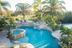 an outdoor pool surrounded by palm trees and water features a slide that leads to a waterfall